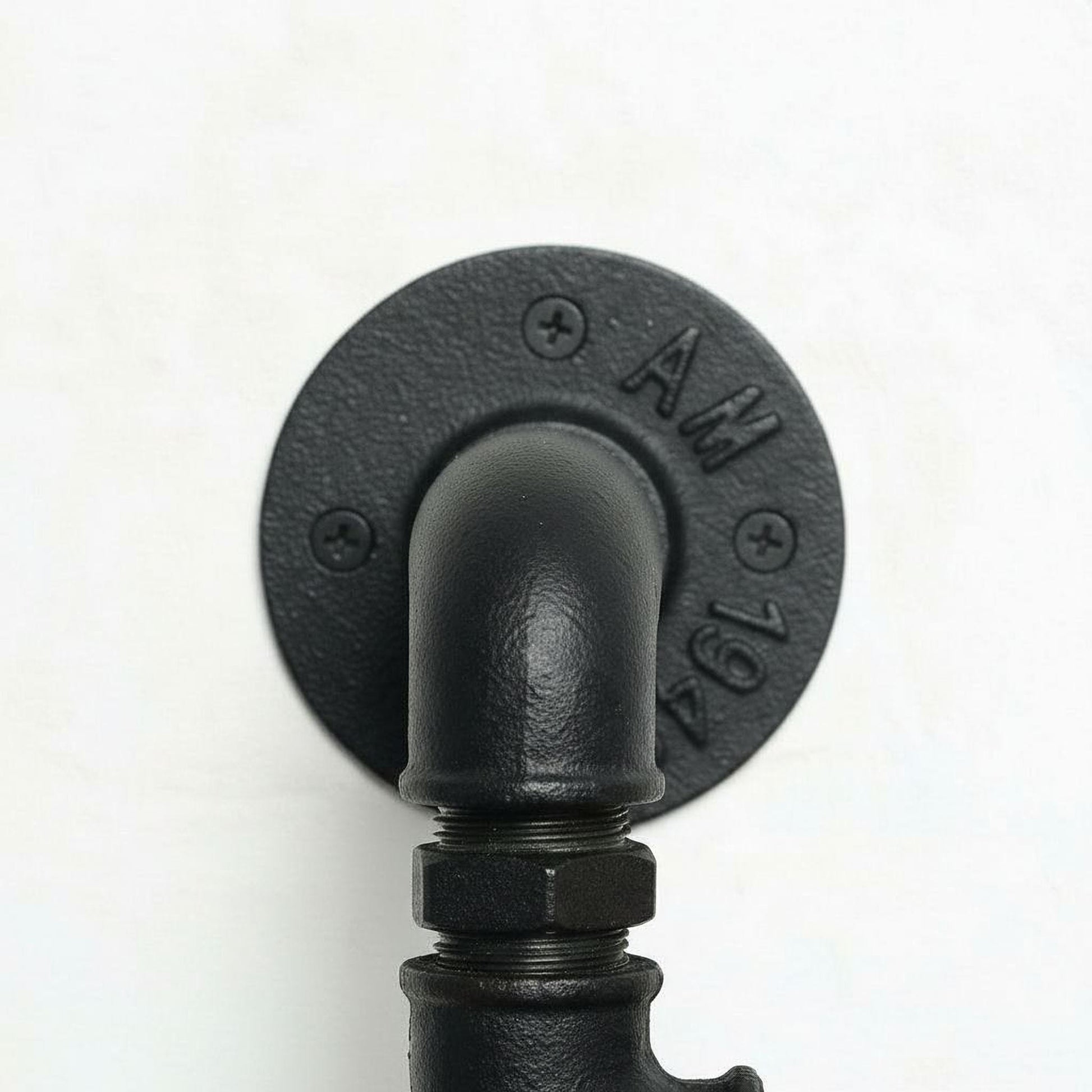 A close-up view of a black pipe or pipe fitting mounted on a wall, with the pipe's curve and the round plate with the number "AM" visible.
