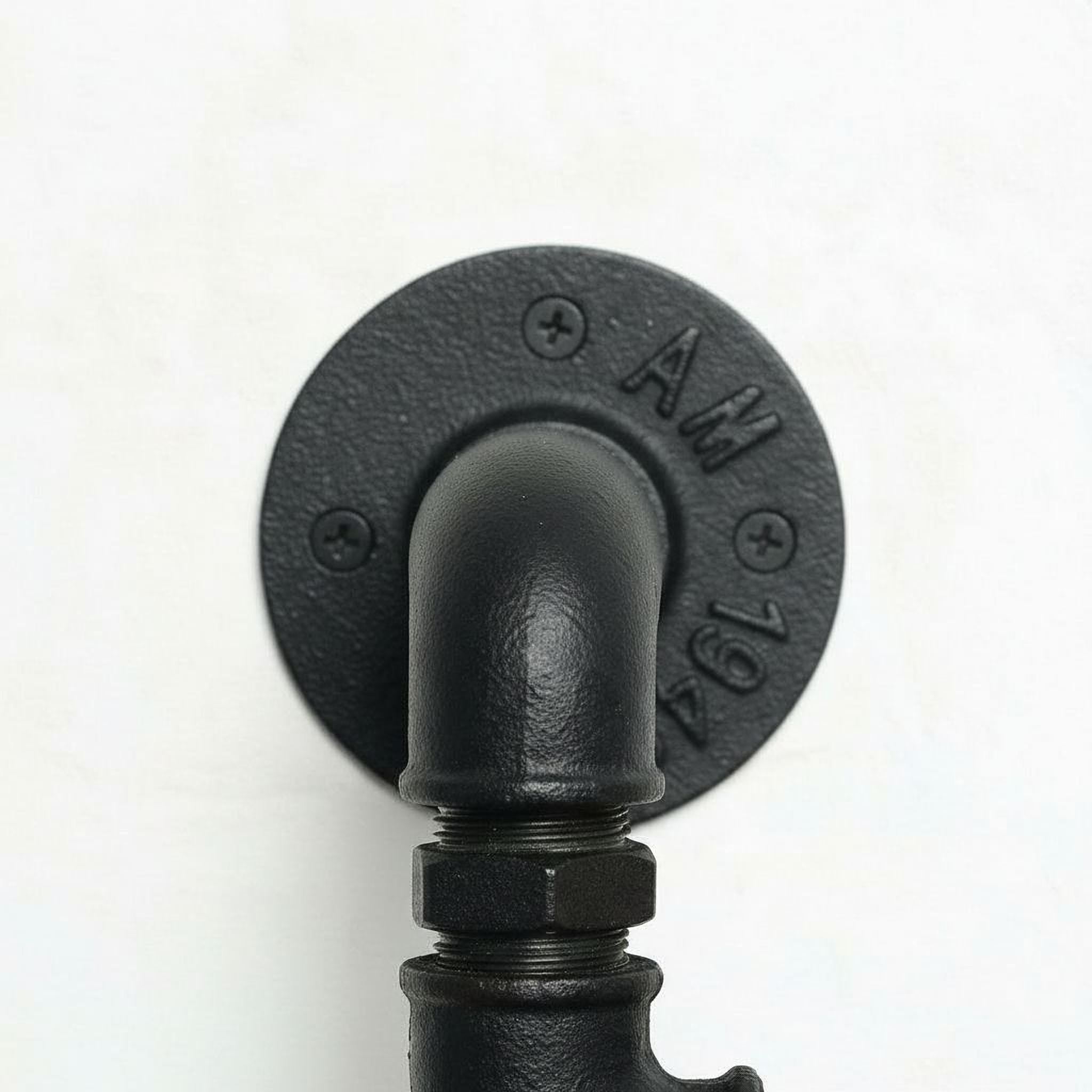 A close-up view of a black pipe or pipe fitting mounted on a wall, with the pipe's curve and the round plate with the number "AM" visible.